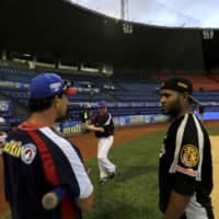 Anthony DeFrancesco (center), son of Tiburones head coach Tony DeFrancesco (left), practices his swing as his father speaks with a player prior to a Venezuela Winter League game against rival Leones at Estadio Universitario in Caracas in November 2013.