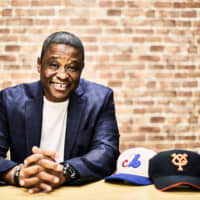 Former Central League MVP Warren Cromartie poses with the hats of his former teams, the Yomiuri Giants (right) and Montreal Expos.