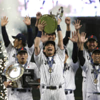 Samurai Japan infielder Nobuhiro Matsuda lifts the Premier12 trophy as his teammates celebrate after their 5-3 win over South Korea in the final on Sunday at Tokyo Dome.