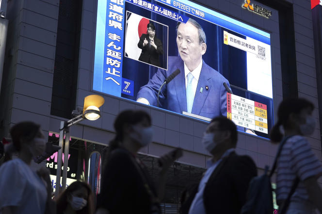 Des gens passent devant un grand écran, tandis que le premier ministre japonais, Yoshihide Suga, s’exprime sur la situation sanitaire du pays, à Tokyo, le 17 juin 2021.