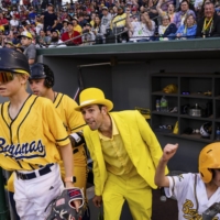 Jesse Cole, center in yellow tux, the owner of the Savannah Bananas, in the dugout for a road game with the Kansas City Monarchs, in Kansas City, May 7, 2022. TikTok choreography, dancing umpires, a ballet-trained first-base coach: This collegiate summer league team has amassed a big following by leaning into entertainment. | SHAWN BRACKBILL / THE NEW YORK TIMES 