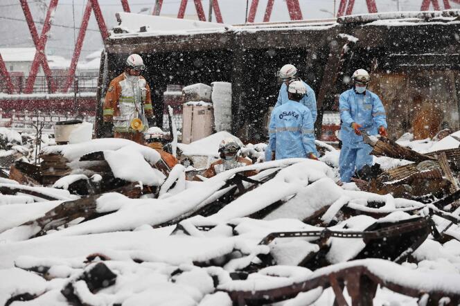 Des pompiers recherchent des personnes disparues dans les ruines calcinées du marché de Wajima alors que la neige recouvre une partie de la zone sinistrée, le 8 janvier 2024, une semaine après le tremblement de terre.